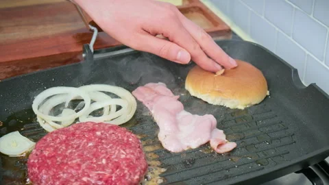 Toasting bread buns on a grilling pan along with beef burger ingredients in 4K. Stock Footage 153753959