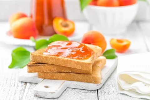 Toasts of bread with apricot jam and fresh fruit with leaves on white woode.. Stock Photos