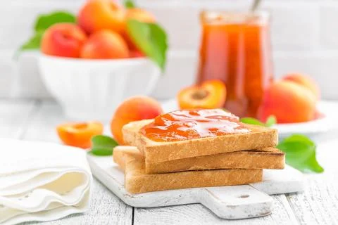 Toasts of bread with apricot jam and fresh fruit with leaves on white woode.. Stock Photos