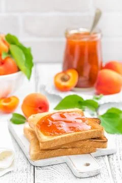 Toasts of bread with apricot jam and fresh fruit with leaves on white woode.. Stock Photos