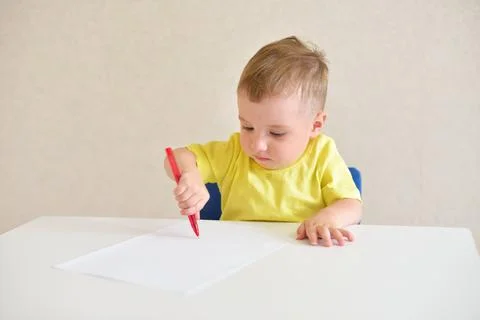 Todder boy plays draws on a piece of paper with a red pen sitting at a white  Stock Photos