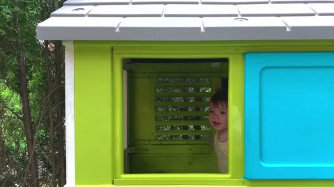 Toddler admiringly peeks out of the window of the playhouse on the playground Stock Footage 154277058