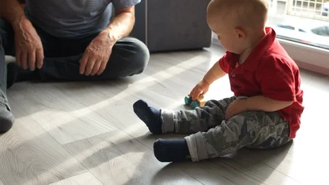 Toddler and an elderly man are playing with a wooden toy car on the floor. Happy Stock Footage 121276953