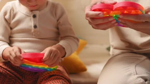 Toddler boy and his mom plays multi-colored toy antistress pop it Видео 199057177