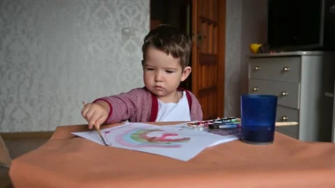 Toddler boy artist sits at the table with art supplies paints and draws. Stock Footage 171381499