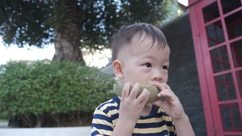 Toddler boy biting / eating fruit (melon) outdoor Stockbeeldmateriaal 98629624