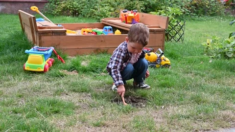 Toddler boy digs the ground for play on the background of the sandbox with cars. Stock Footage 151526811
