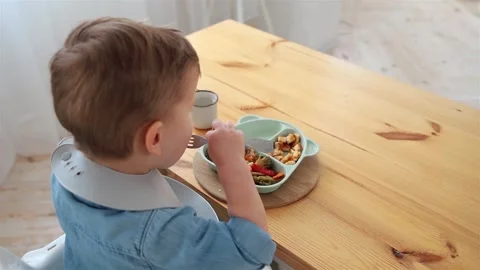 Toddler boy eats vegetables on his own using a fork, view from the back. Self Stock Footage 234396002
