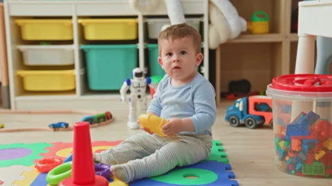 Toddler boy holding yellow stacking toy in both hands, sitting on colorful .. Stock Footage 337388869