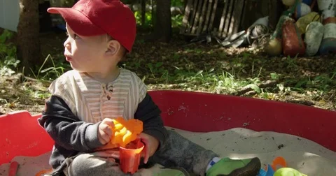 Toddler boy plays in sandbox next to forest Stock Footage