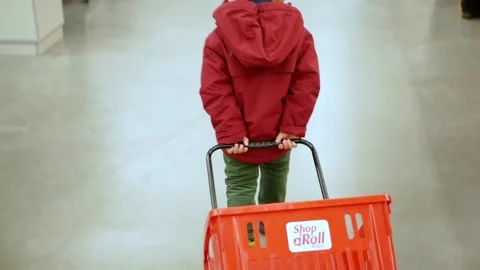 Toddler boy pulls shopping cart and looking around walking through suremarket. Stock Footage 153396896