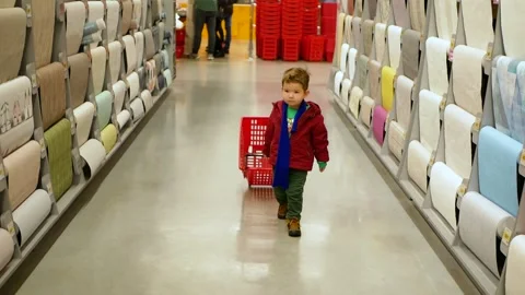 Toddler boy pulls shopping cart and looking around walking in hardware store. Stock Footage 153460416