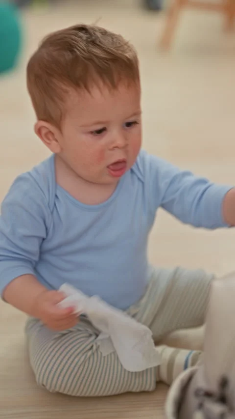Toddler boy seated on floor pulling a wet wipe from a diaper bag zipper whi.. Stockbeeldmateriaal 339210523