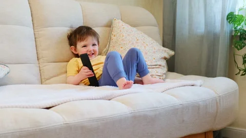 Toddler boy sitting on sofa holding television remote controller. Happy child Stock Footage 343169251