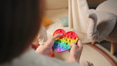 Toddler boy takes a multi-colored toy antistress pop it from his mother Stock Footage 199057471