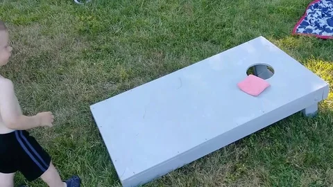 Toddler boy tossing bean bags into a cornhole outdoors having fun playing Stock Footage 93961553