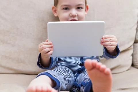 Toddler boy is using a tablet on a couch Stock Photos