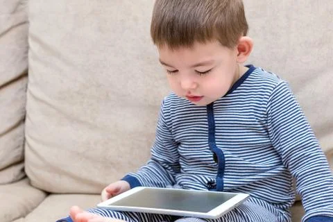 Toddler boy is using a tablet on a couch Foto stock