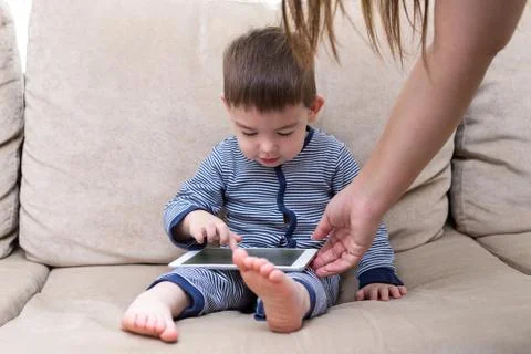 Toddler boy is using a tablet on a couch Stock Photos