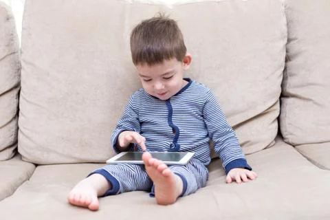 Toddler boy is using a tablet on a couch Stock Photos
