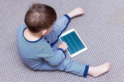 Toddler boy is using a tablet on a couch Stock Photos