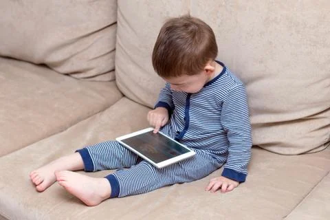 Toddler boy is using a tablet on a couch Stock Photos