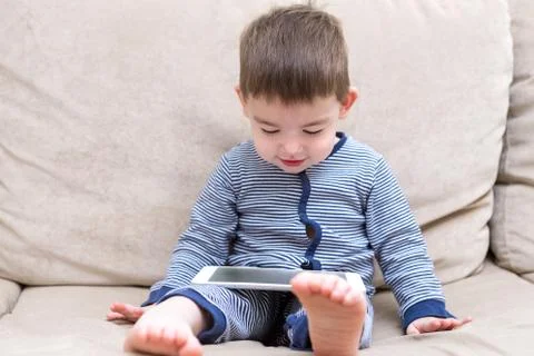 Toddler boy is using a tablet on a couch Stock-Fotos
