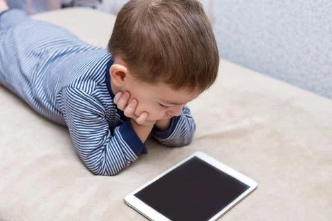Toddler boy is using a tablet on a couch Stock Photos