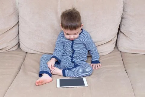 Toddler boy is using a tablet on a couch Foto stock