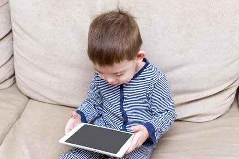 Toddler boy is using a tablet on a couch Foto stock