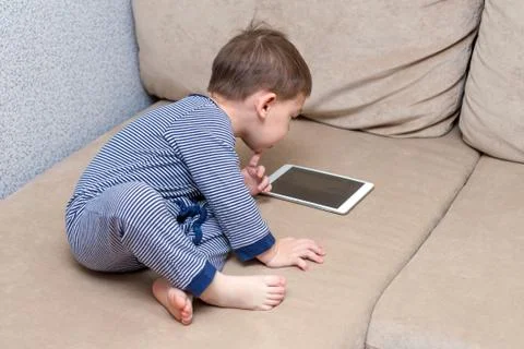 Toddler boy is using a tablet on a couch Stock Photos