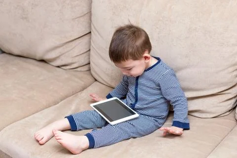 Toddler boy is using a tablet on a couch Stock Photos