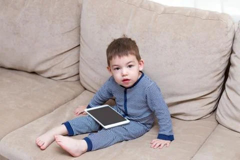 Toddler boy is using a tablet on a couch Stock Photos