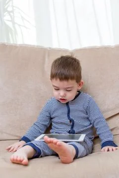 Toddler boy is using a tablet on a couch Stock Photos