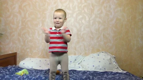 Toddler claps his hands while standing on the bed Stock Footage 137954336