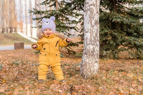 Toddler dressed in a yellow jacket is dancing while standing on autumn leaves Stock Photos