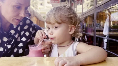 Toddler drinking a berry fruit drink through a straw at an outdoor cafe with mot Stock Footage 341244544