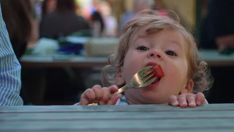 Toddler eating tomato slice from fork during outdoor family meal before mot.. Stock Footage 335691306