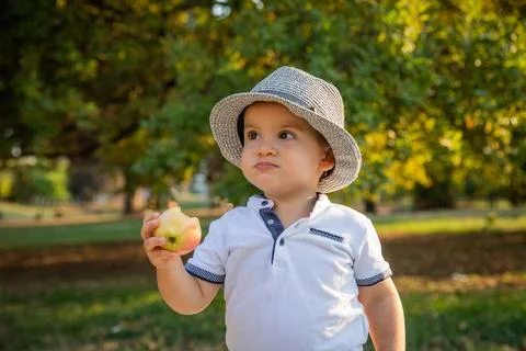 A toddler eats an apple while in a public park, children and healthy lifest.. Foto stock
