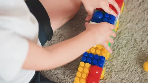 Toddler engaged in stacking vibrant plastic blocks on carpet. Young boy focusing Stock Footage 346201394