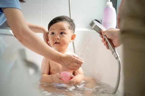 Toddler enjoys bath time while being washed by caregivers in a cozy bathroo.. Stock Photos