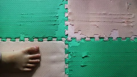 Toddler foot stepping on a damaged interlocking foam puzzle mat Stock Photos