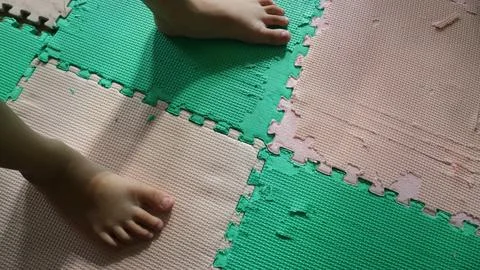 Toddler foot stepping on a damaged interlocking foam puzzle mat Stock Photos