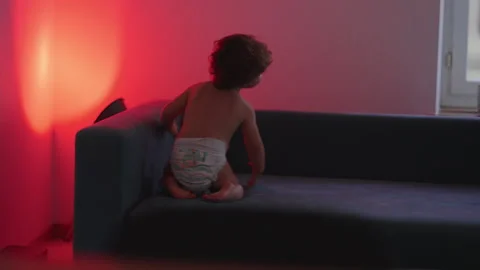 Toddler getting up from couch at home, highlighting gross motor development.. Stock Footage 340425189