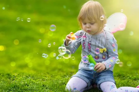 Toddler girl with butterfly wings having fun in the park, blowing soap bubbles Stock Photos