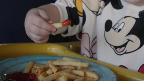 Toddler girl eats French fries with ketchup sitting in chair Stock Footage