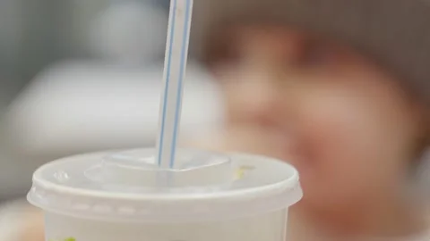Toddler girl in hat eats fast-food with hands and drinks through a straw. Stock Footage 130314276