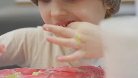 Toddler girl in hat eats fast-food with hands and drinks through a straw Stock Footage 130396375
