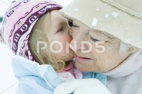 Toddler Girl Kissing Grandmother On Cheek, Both Dressed In Winter Clothing,