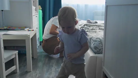Toddler girl taking first steps at home while mother stays nearby Stock Footage 336302595